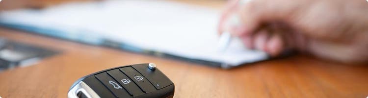 car key fob next to hand signing paperwork