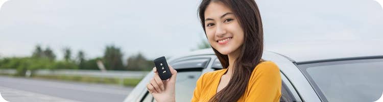 woman holds key fob in front of new car