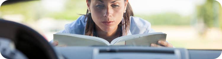 woman reads car manual over open car hood